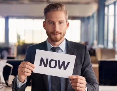 Firefly executive man looking straight with now sign; blurry office background 62833